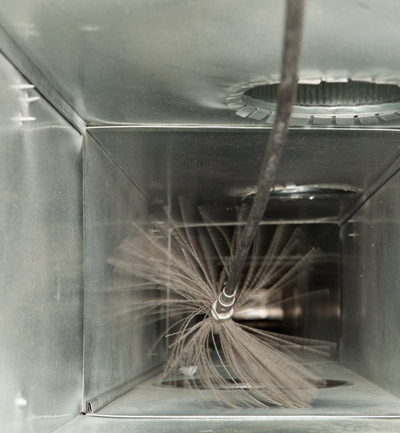Close-up interior view of a rotary brush removing dust and debris from inside a rectangular HVAC air duct.
