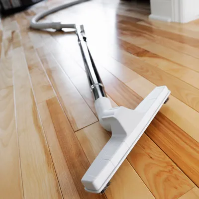 Central vacuum floor tool cleaning a hardwood floor with a hose extended through a residential hallway.